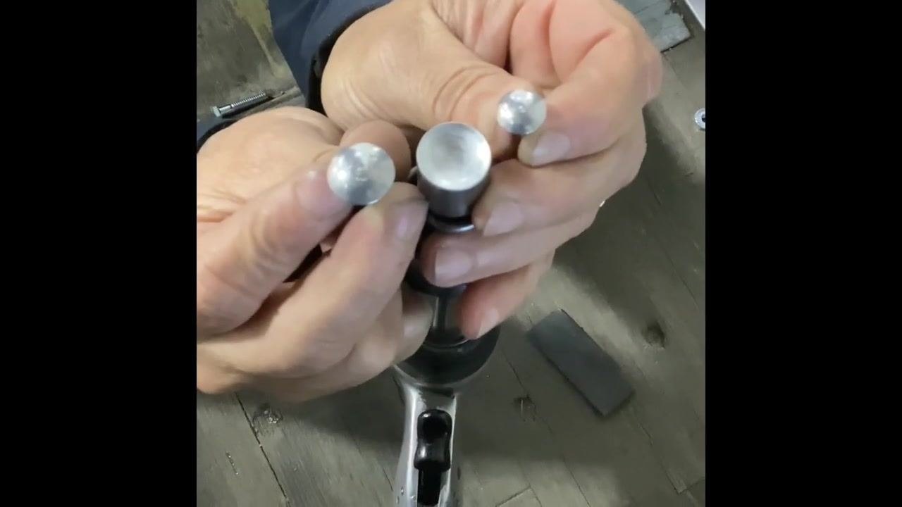 Hands holding three different rivet heads and an air hammer with a rivet head bit, showing differences in size and shape.