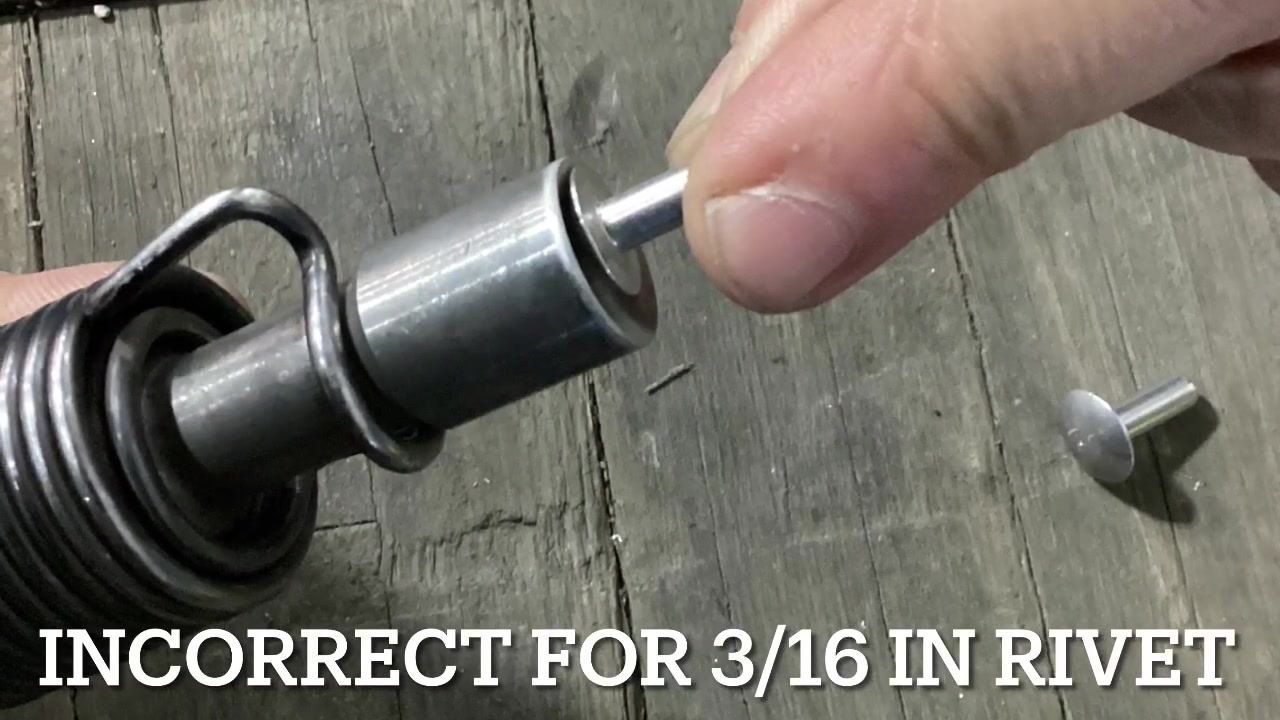 Hands holding two different-sized rivets and an air hammer bit, showing a direct comparison of rivet head sizes above a workbench.