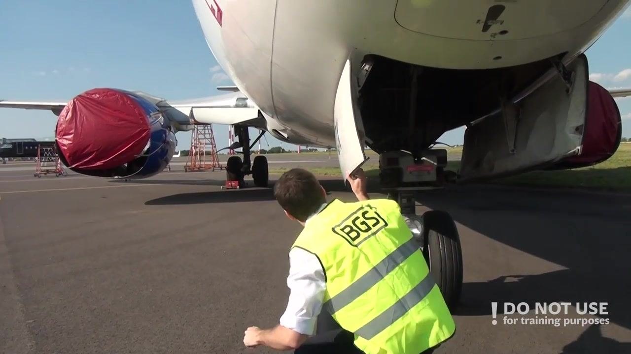 Person reaching up to inspect the underside of the aircraft's nose area near the right front fuselage.