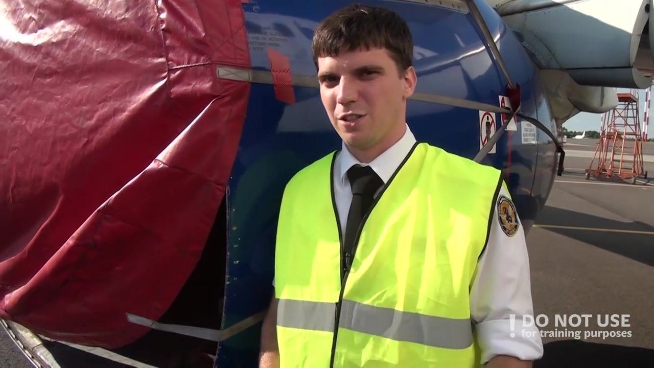 A person in a high-visibility vest stands in front of an engine nacelle with a red cover, explaining the inspection process. The engine is not present.