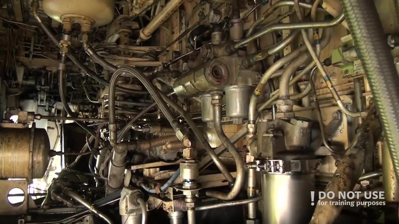 Hand gesturing inside the main wheel well, showing hydraulic lines, valves, and the APU fire handle.