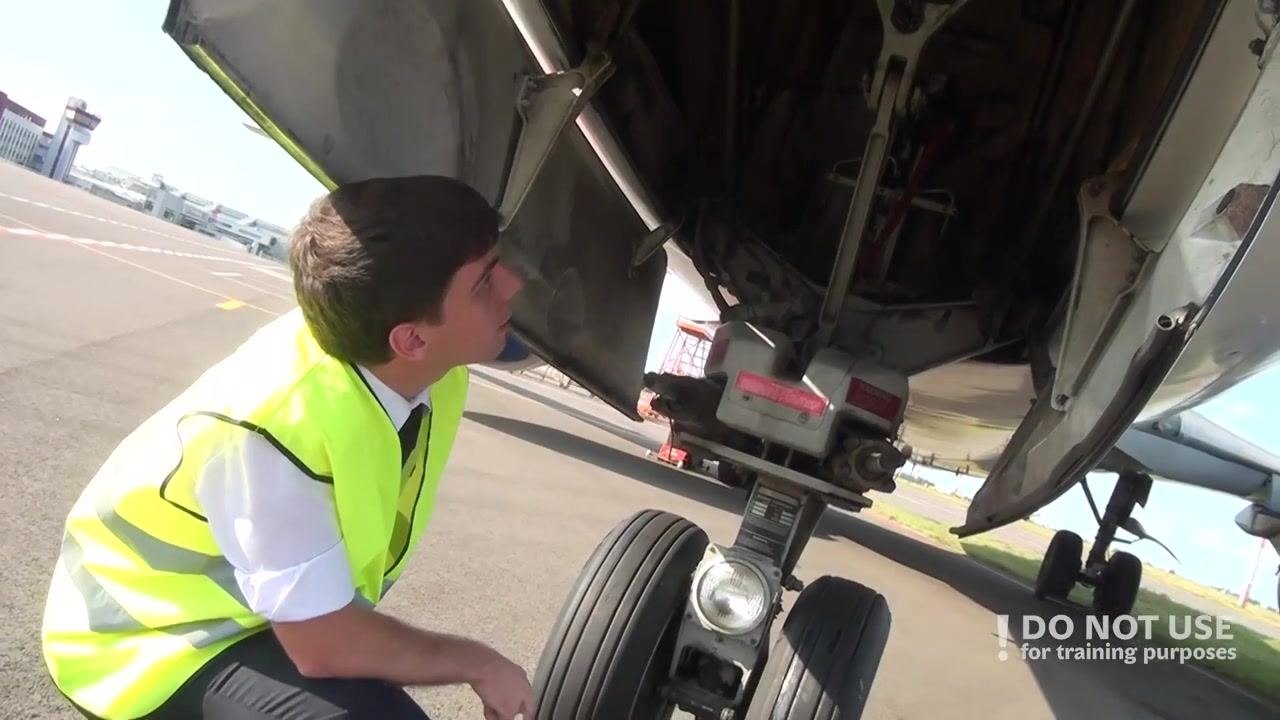 Person crouched near the nose gear, inspecting the underside of the aircraft with the nose gear doors open.