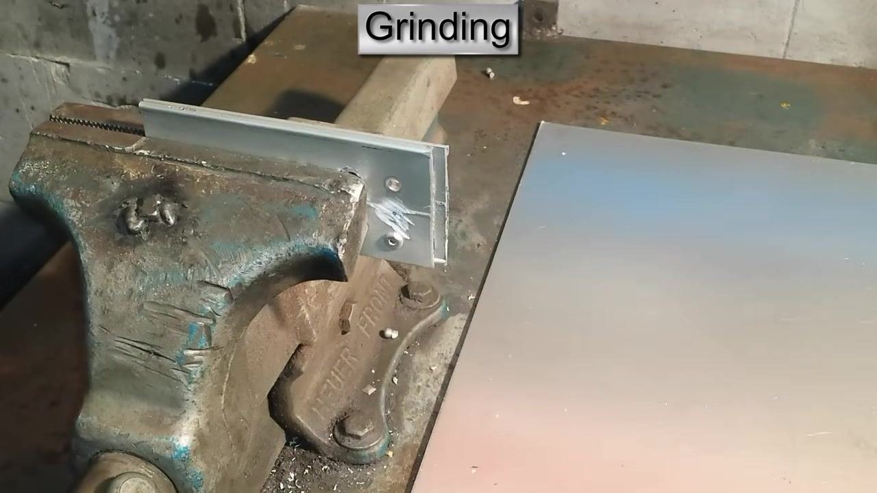 A finger pointing to a rivet head, with an angle grinder positioned nearby. On-screen text: "Grinding."