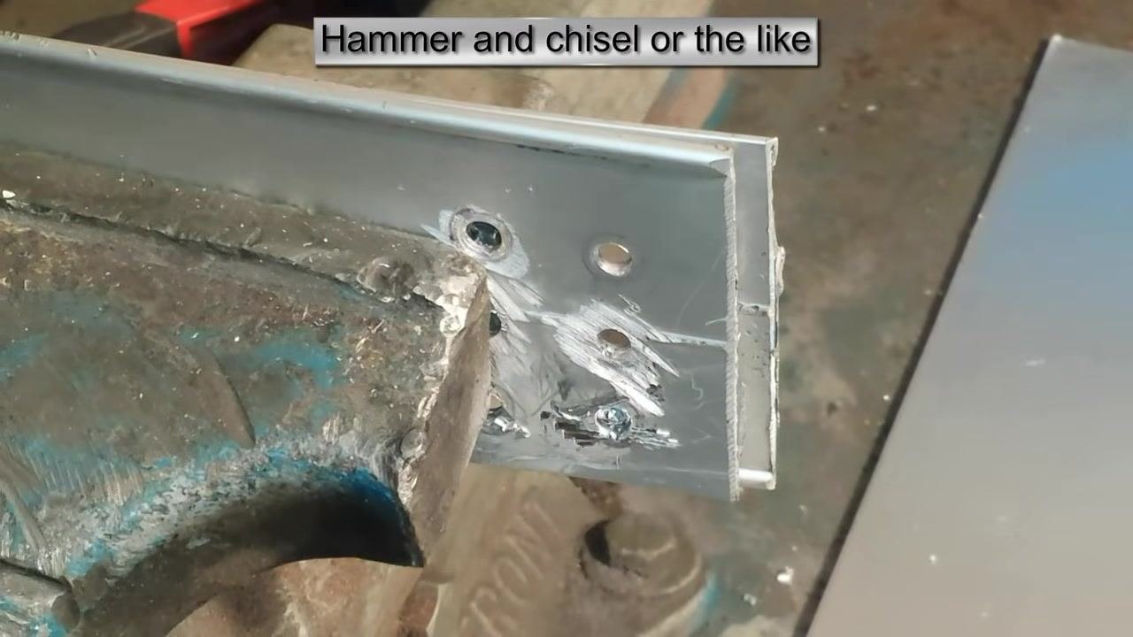 The workpiece after all rivet heads have been removed, showing clean holes and tool marks, with the L-bracket still clamped in the vise. On-screen text: "Hammer and chisel or the like."