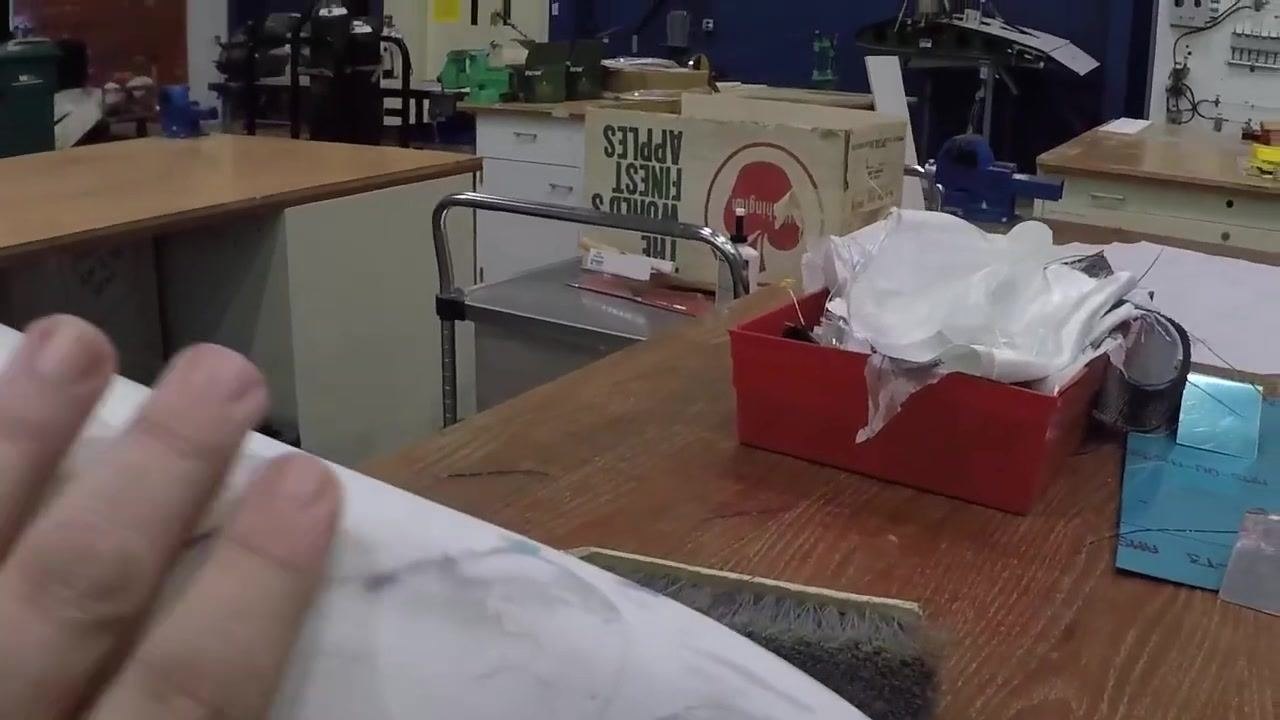 A hand smooths a white curved object with visible repair marks on a wooden workbench, with workshop supplies in the background.