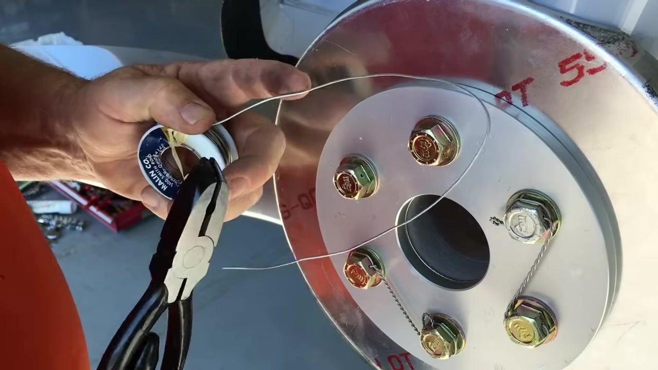Cutting a measured length of 0.041" steel safety wire from the spool using pliers, with the propeller hub and bolts visible