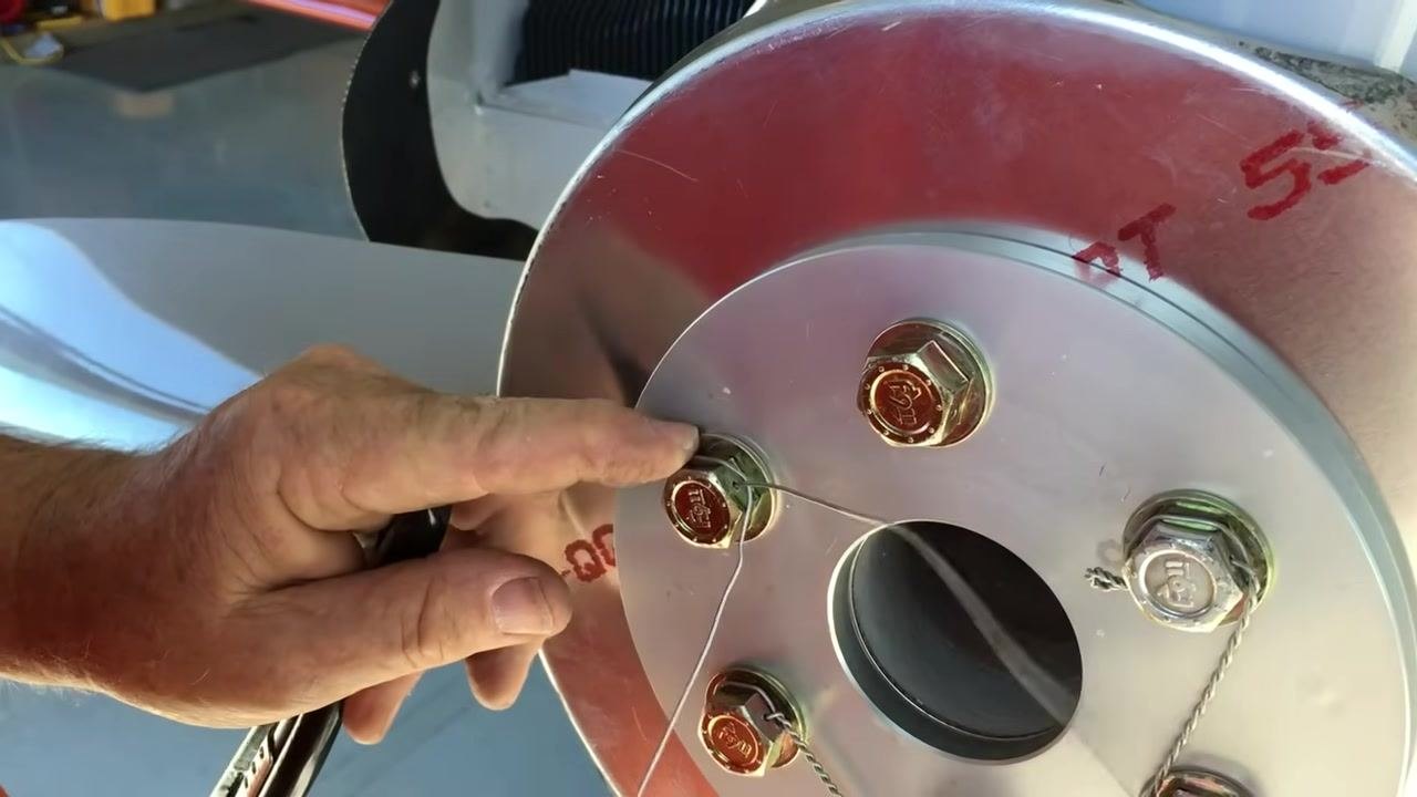 Folding the tag end underneath and pulling the safety wire tight around the bolts, preparing for twisting