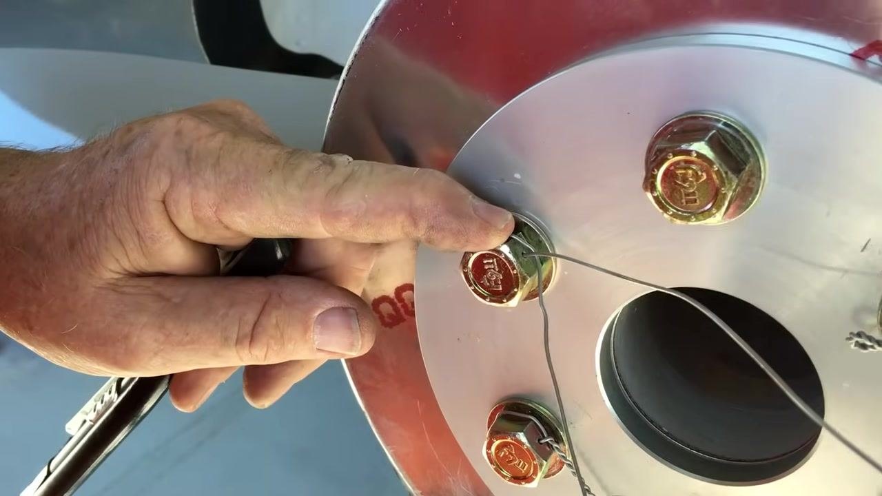 Positioning the safety wire at the entry hole of the next bolt, preparing to use safety wire pliers