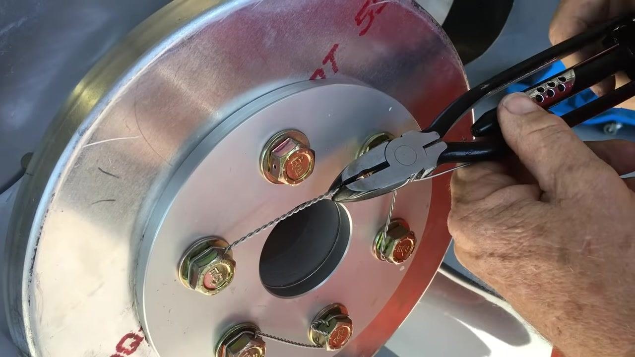 Applying safety wire pliers to the wire, pulling it tight between the bolts on the propeller hub