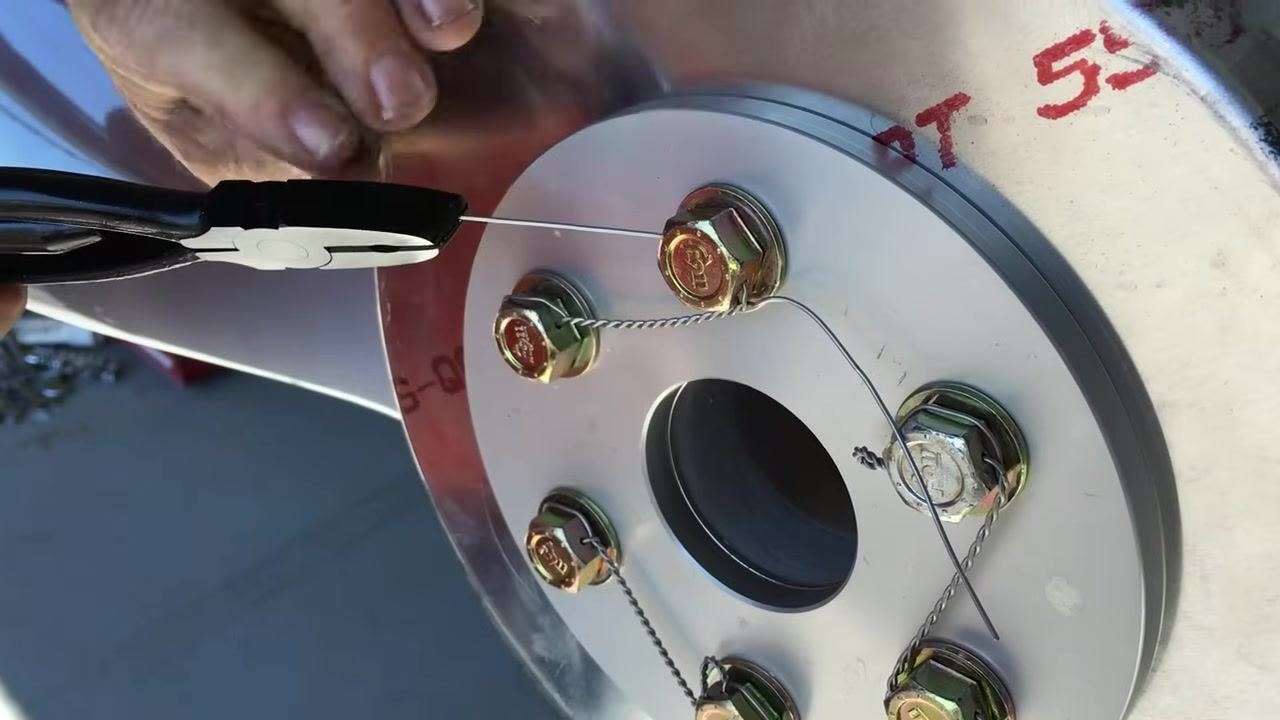 Using safety wire pliers to pull the wire tight after threading it through the bolt head