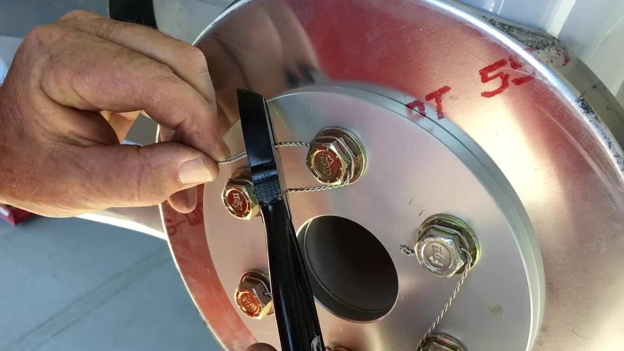 Hand-twisting the tag end (pigtail) of the safety wire in the opposite direction, using pliers for precision, with the wire aligned to the bolt hole