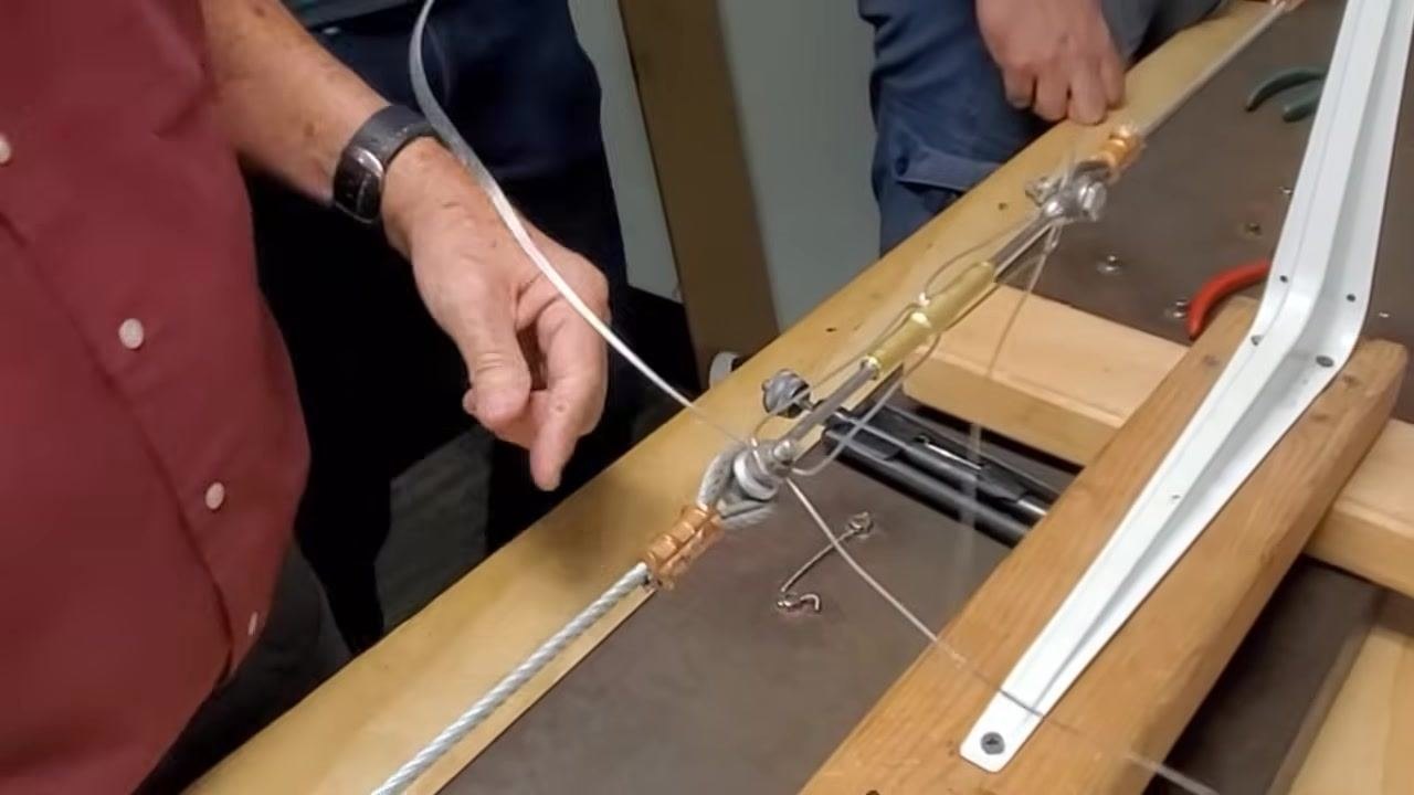 A person inspects the completed double wrap, with both wires clearly visible and routed in opposite directions through the turnbuckle horns.