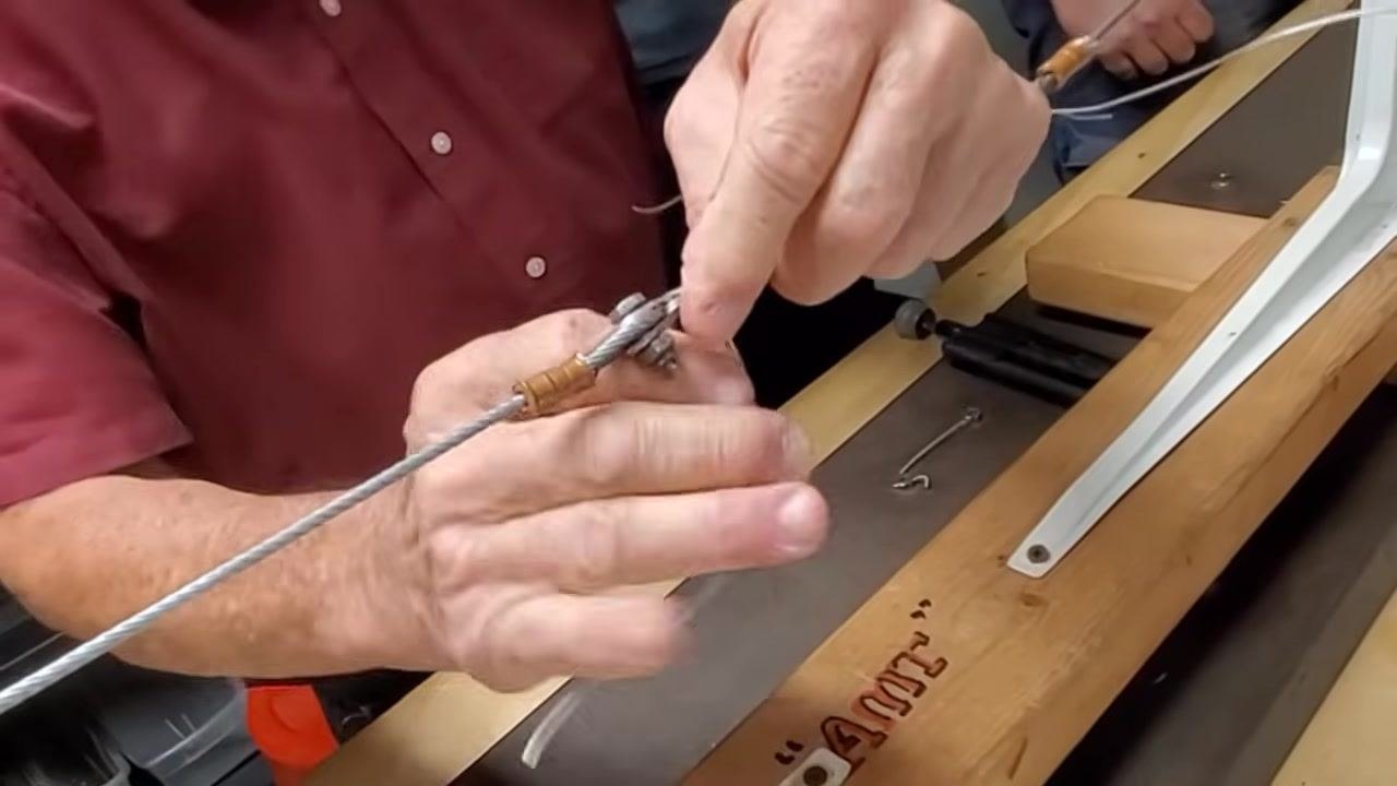 A cable assembly with both ends of the safety wire twisted, tools on the workbench, and hands visible, indicating the completion of the twisting process.