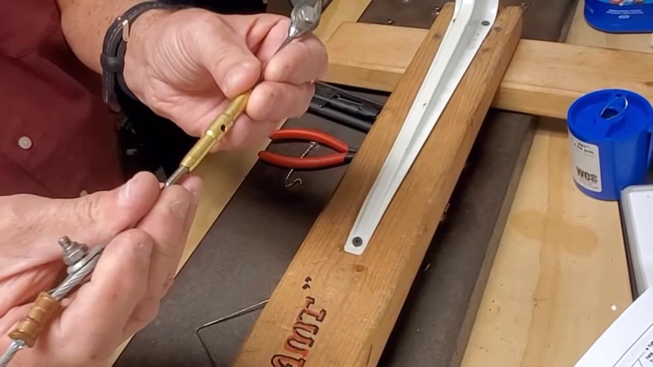 Hands align and start screwing in the second brass turnbuckle onto the cable, ensuring the cable does not twist.