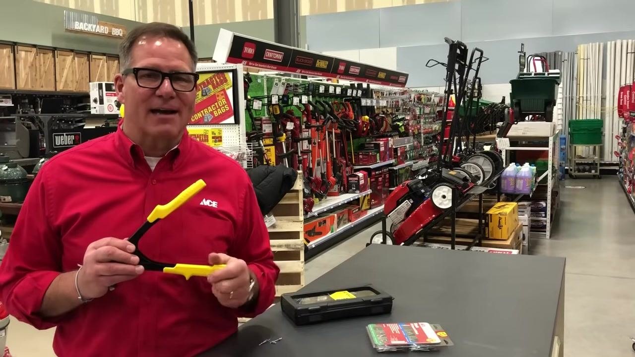 Presenter in a red ACE shirt holding a rivet gun, smiling and speaking to the camera in a hardware store aisle. The counter displays a rivet gun case and a package of assorted rivets. The background includes lawn equipment and hardware supplies.