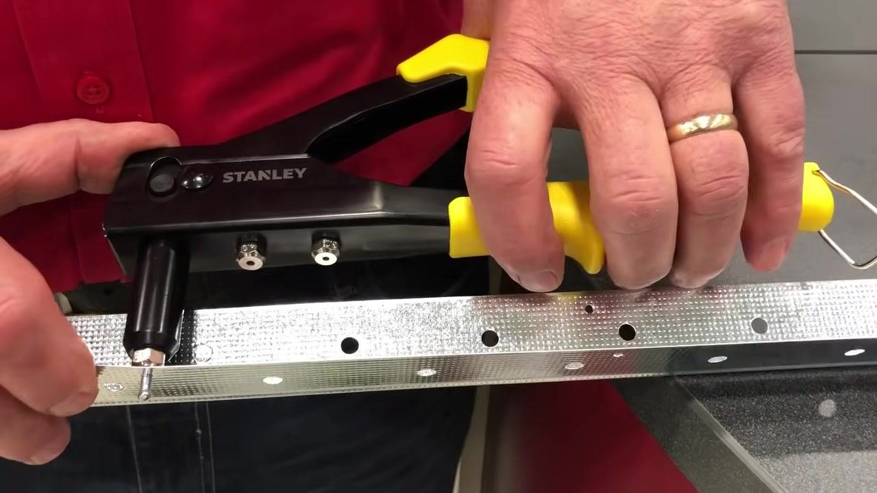 Yellow-handled rivet gun and a rivet being prepared for insertion above the metal strip