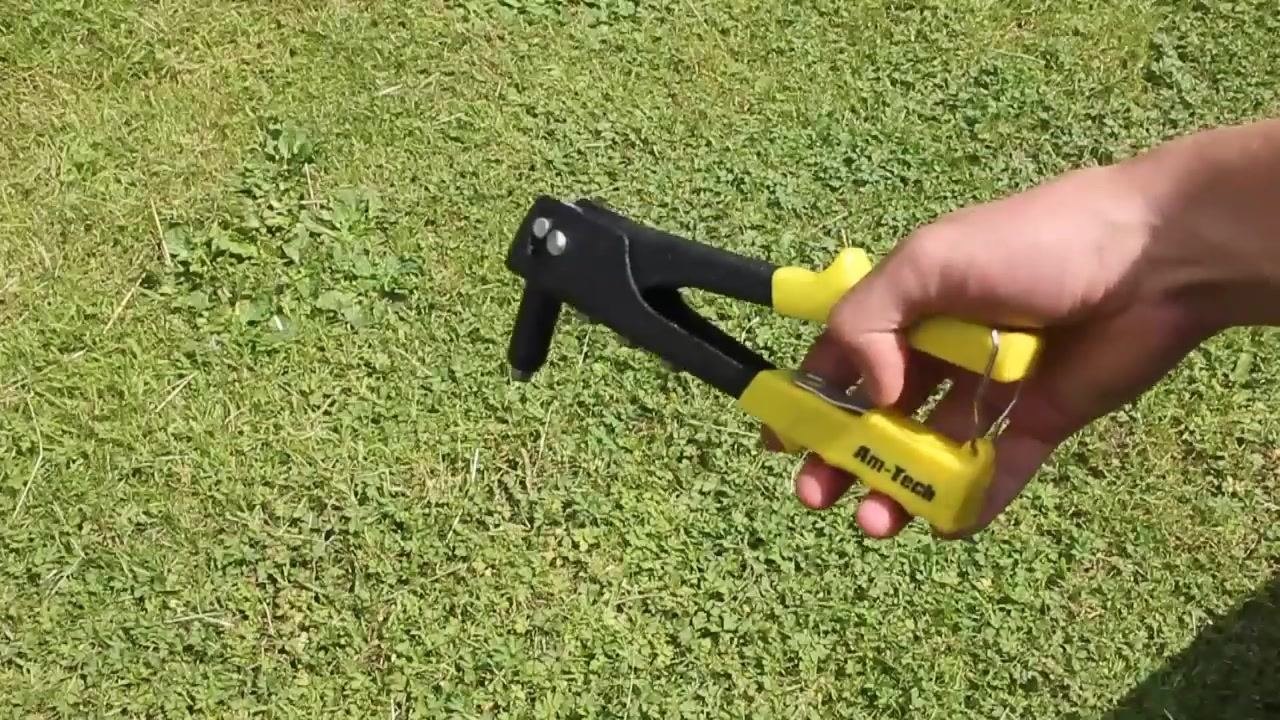 A hand holding a yellow and black Am-Tech pop riveter over grass, showing the tool's general shape and handle design.