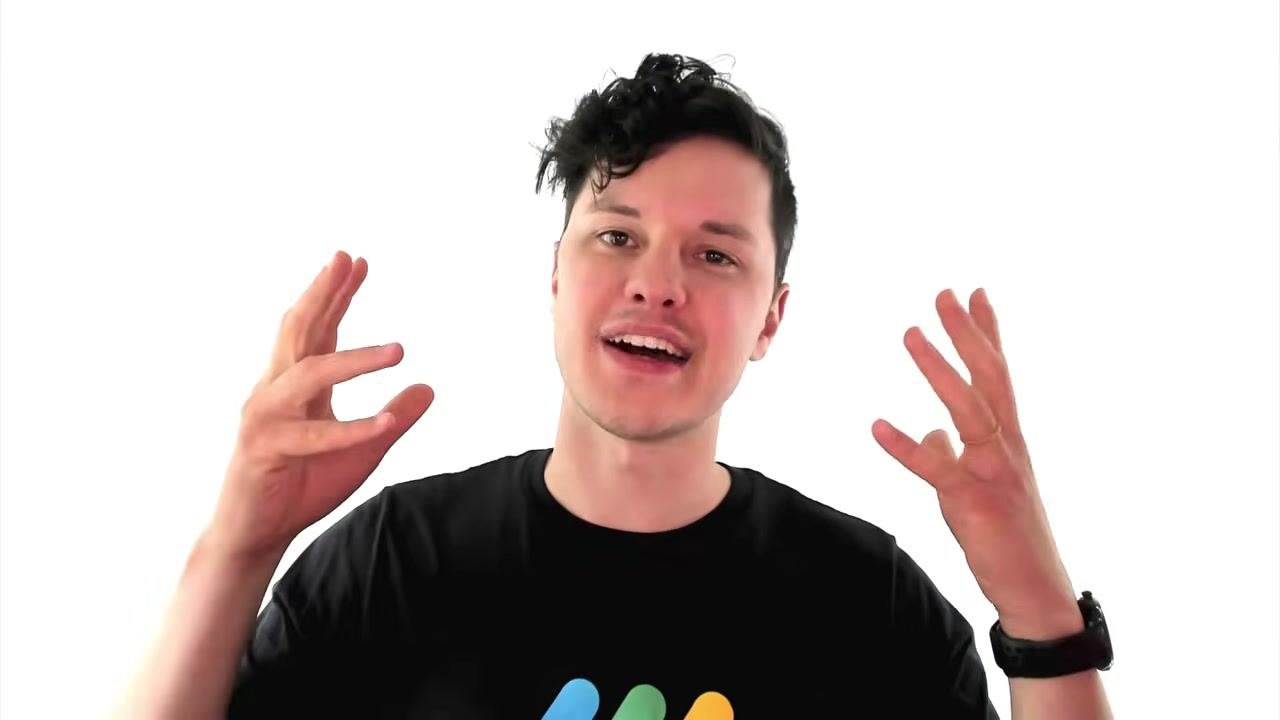 Presenter in a black t-shirt with a colorful logo, speaking directly to the camera against a plain white background. No visible UI elements or on-screen text.