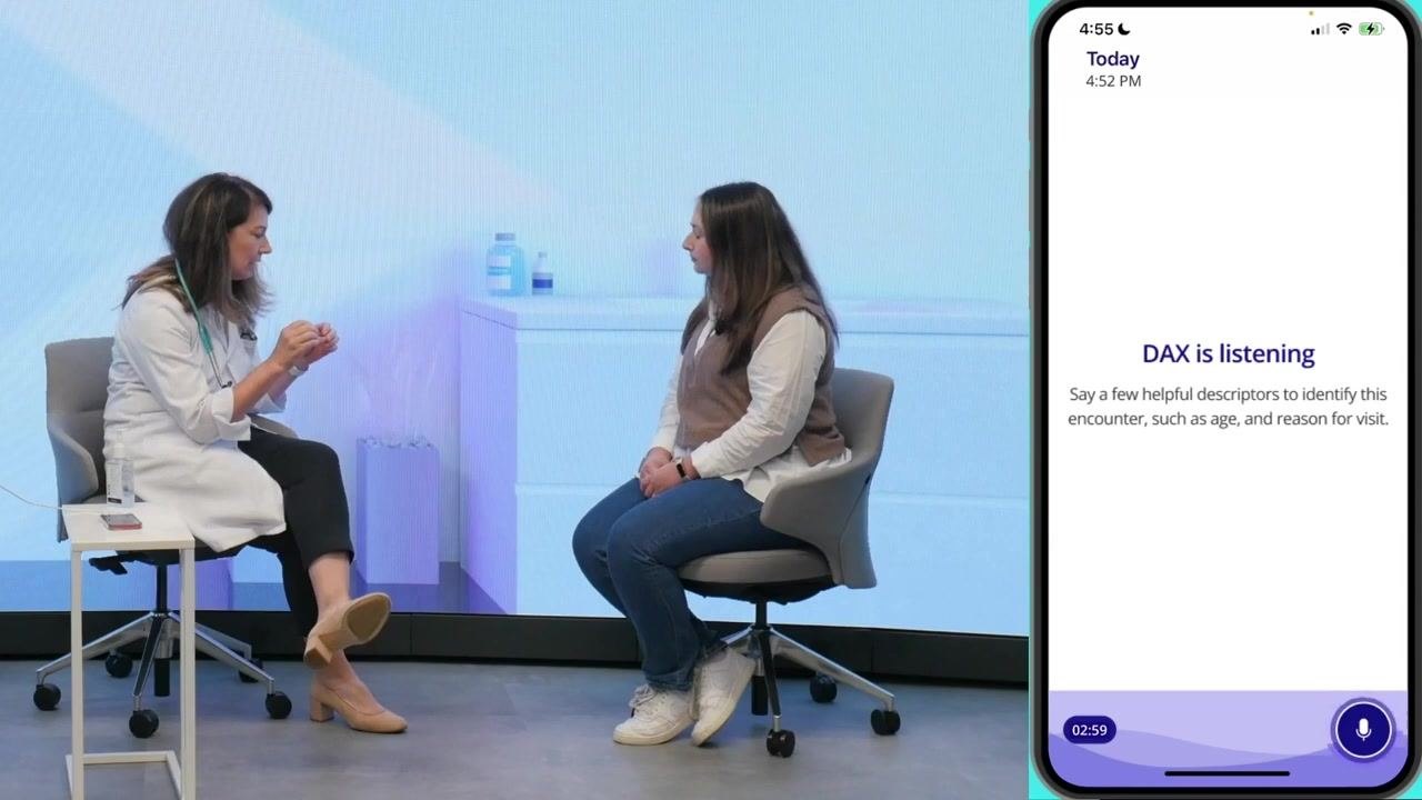 Clinician and patient facing each other in the exam room, with the phone screen showing "DAX is listening" and the timer running