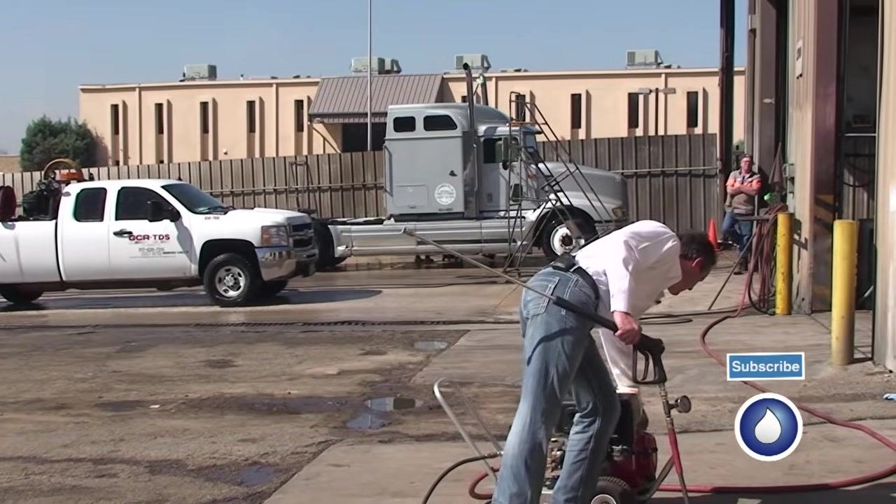 The spray gun and gauge are held while explaining troubleshooting, with the outdoor work area visible.