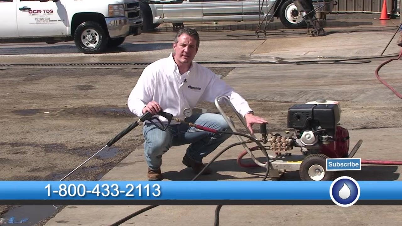 One hand rests on the unloader while the other holds the spray gun, with the test gauge visible on the pressure washer.