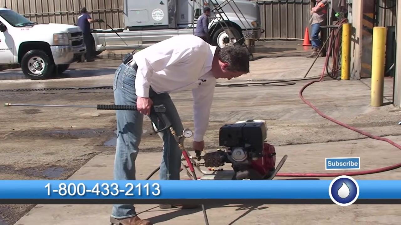 The spray gun is held with an attached pressure gauge clearly showing the reading, with the outdoor work area visible.