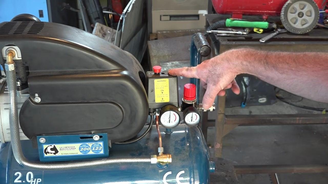 Close-up of the yellow warning label on the pressure switch, reading the factory-set safety warning and ON/OFF instructions, with the red regulator knob visible