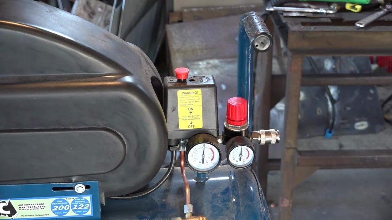 Compressor controls and gauges, including the warning label, red ON/OFF button, and red regulator knob, with a clear view of the full setup