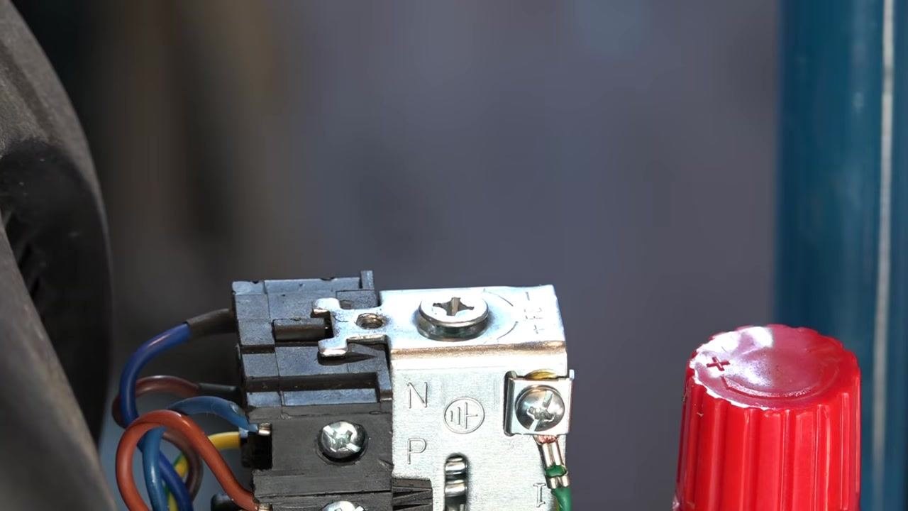 Close-up of the pressure switch adjustment screw, Phillips head, with visible markings and wiring, and the red regulator knob to the right