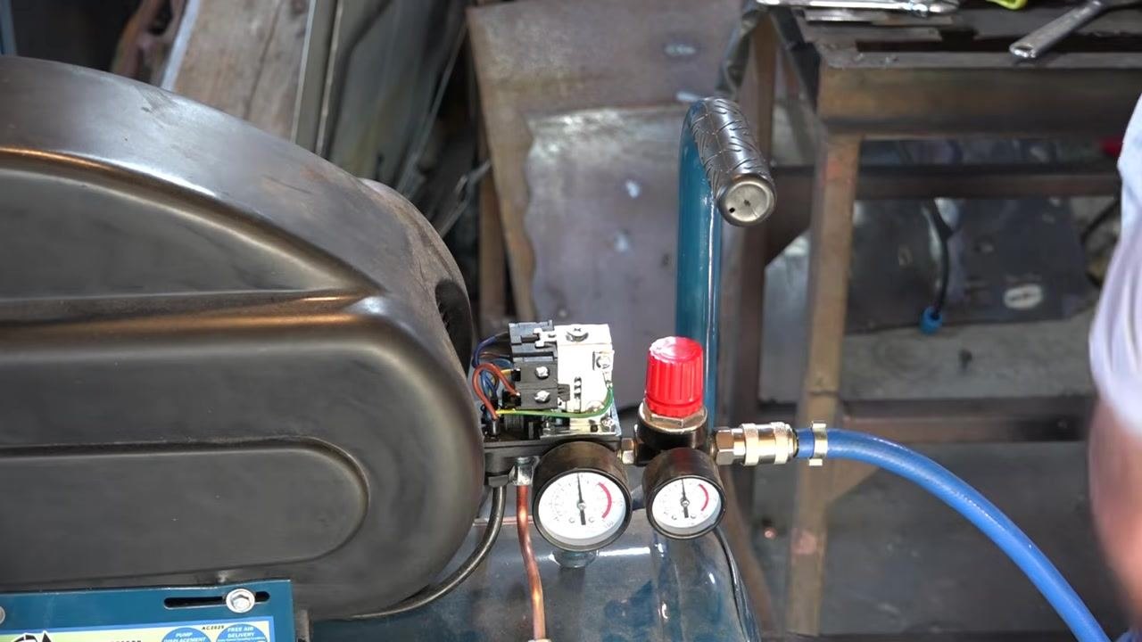 Compressor with a blue air hose attached, positioned to drain air, with gauges and regulator visible
