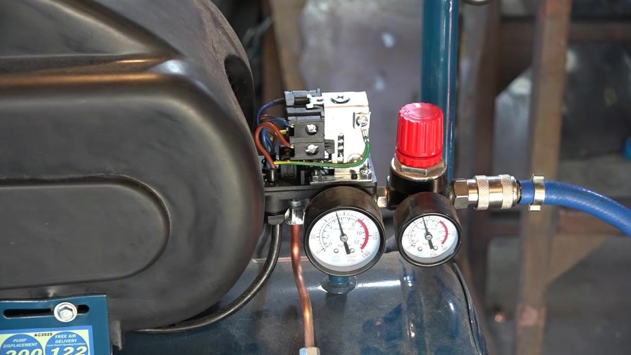 Close-up of compressor gauges showing tank pressure just under 90 psi, with the red regulator knob and wiring visible