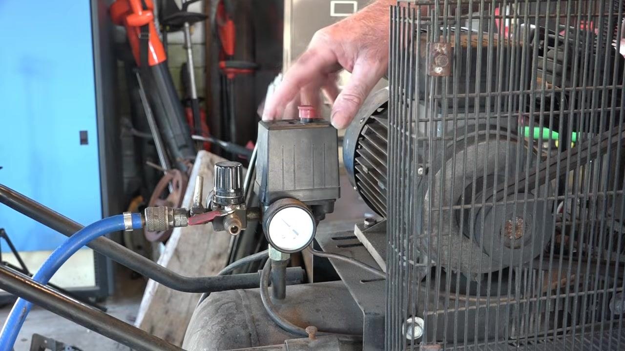 Workshop view of an old air compressor with tools and equipment nearby, showing the pressure gauge and adjustment assembly
