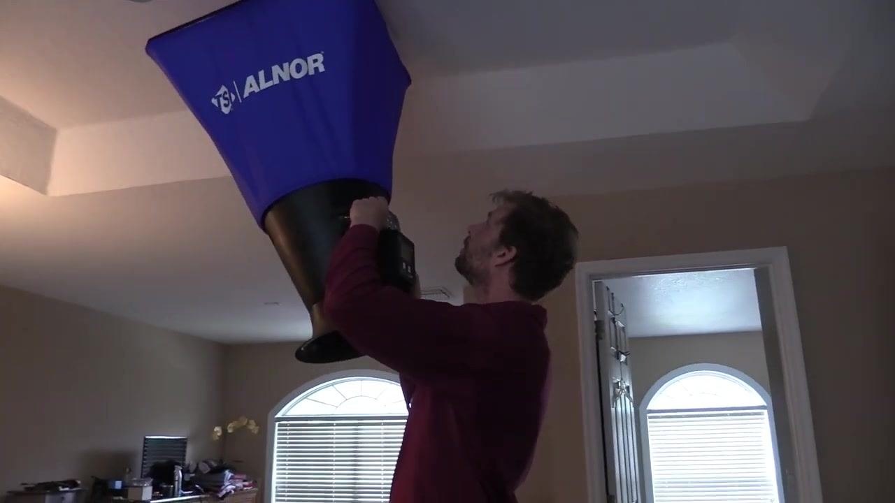 A person stands under a ceiling vent, holding the flow hood in place while the damper is adjusted.