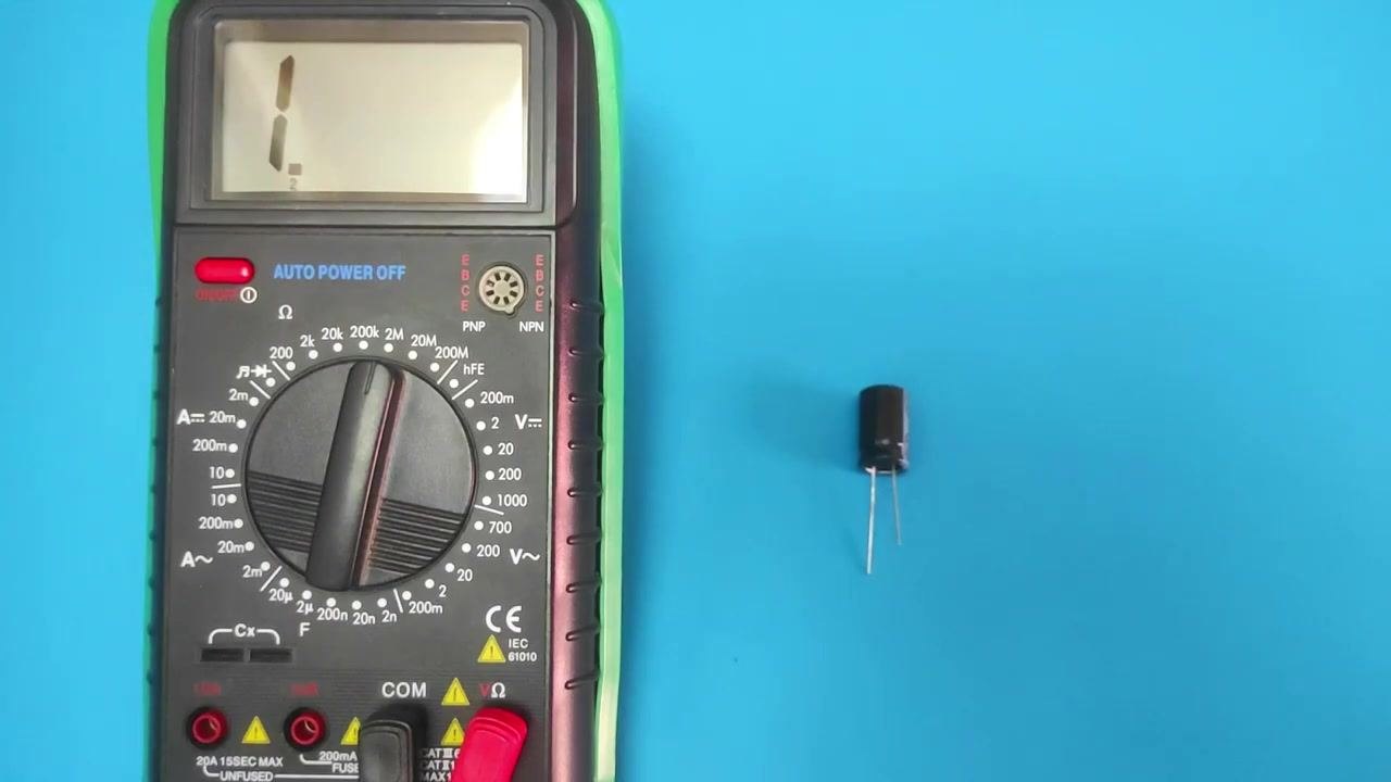 A digital multimeter set to the 2 megaohm (2MΩ) resistance range, placed next to a single electrolytic capacitor on a blue background.