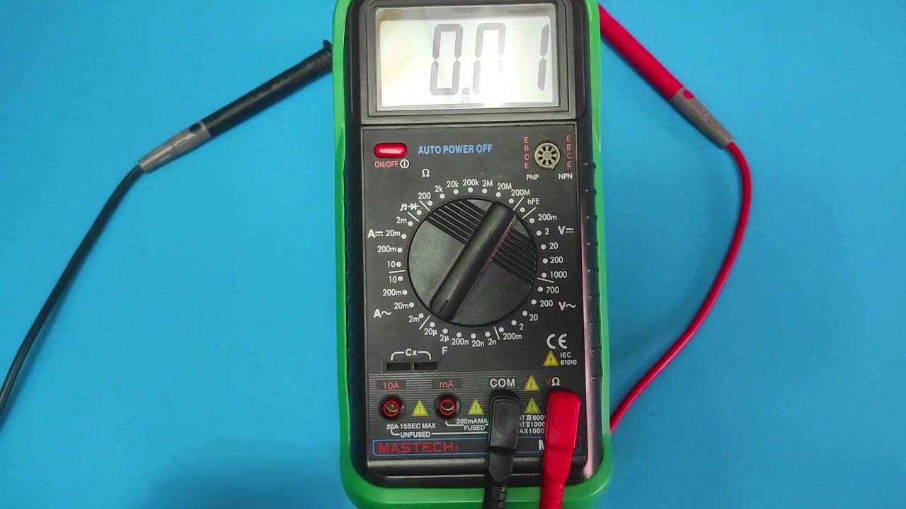 A digital multimeter on a blue surface with probes attached, displaying "0.01" while set for capacitance measurement.