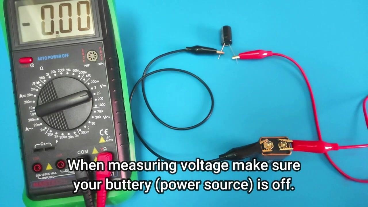 A digital multimeter set to a voltage range above 9V, with the battery and capacitor still connected via jumper wires.