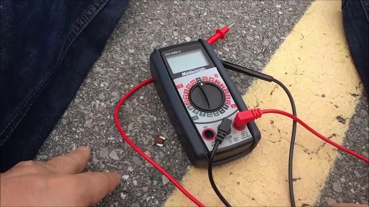 A digital Mastercraft multimeter rests on the ground with the red and black test leads connected, ready for use.