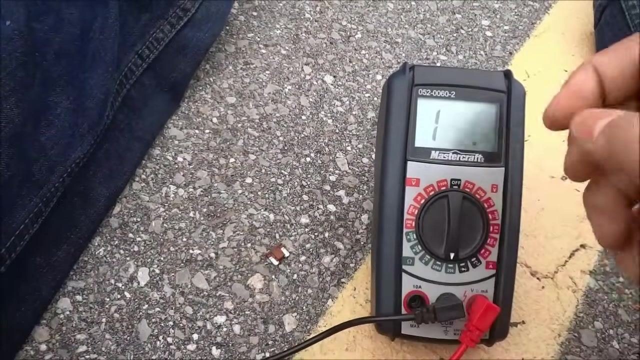 A hand turns the dial of the multimeter to the ohms (Ω) setting to prepare it for continuity testing.