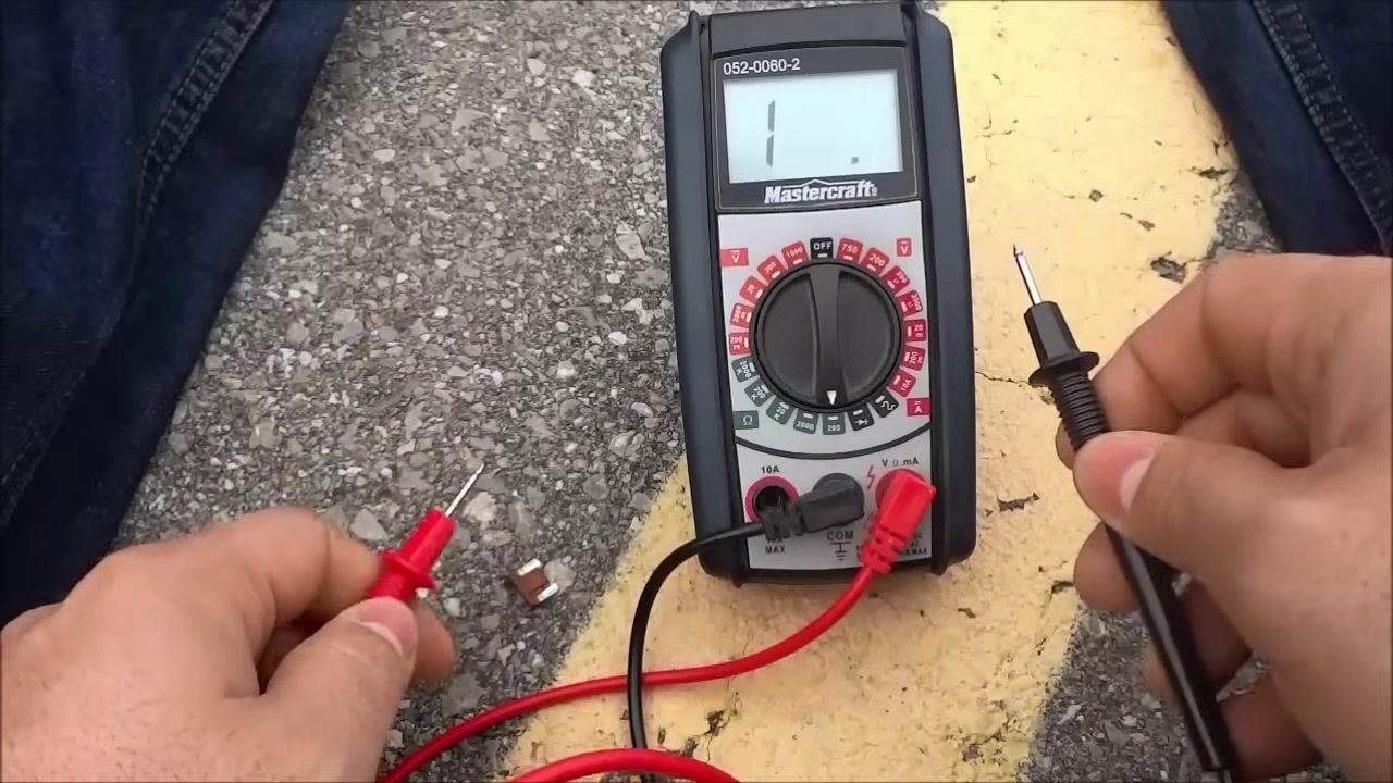 Hands hold the red and black test leads, positioned to test a component for continuity.