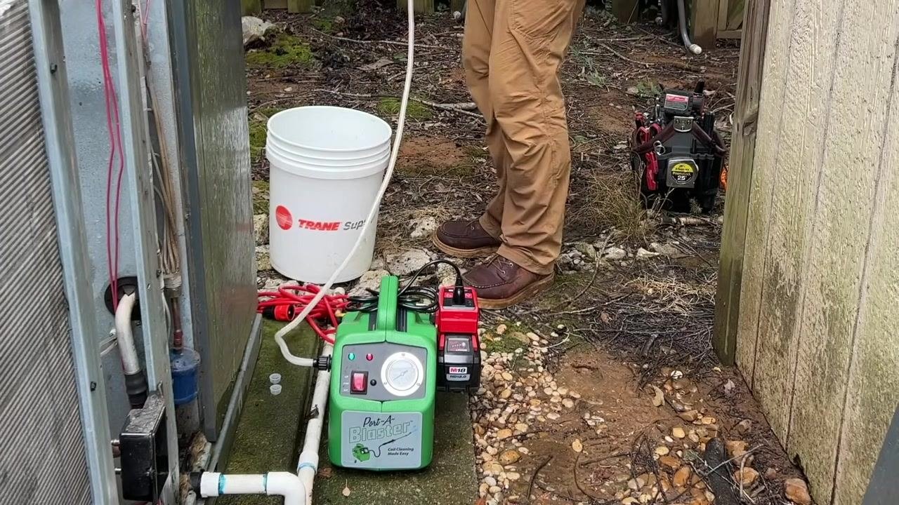 A technician stands next to the Port-A-Blaster, bucket, and connected hoses, prepared for operation.