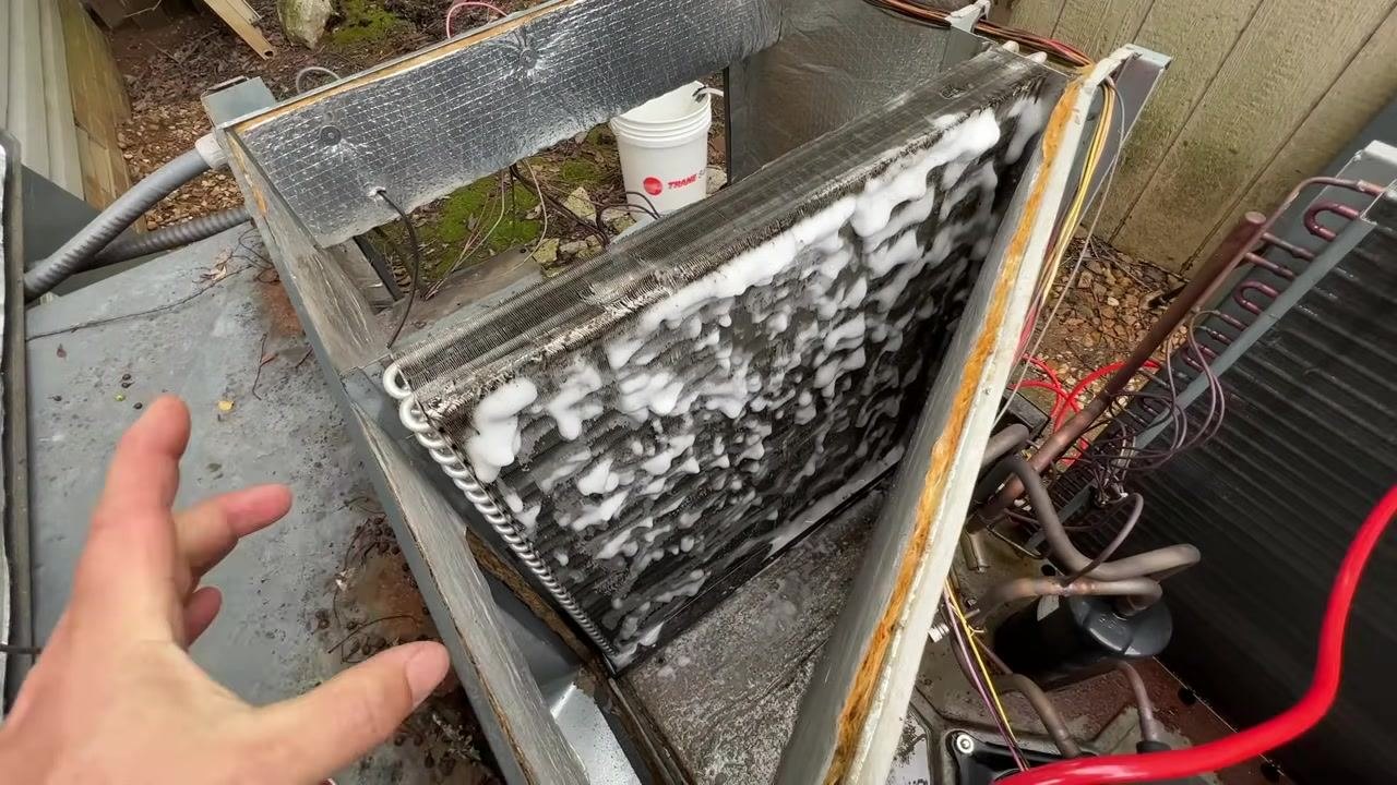 A close-up shows foam cleaner applied to both sides of the coil, with a technician's hand pointing for inspection.