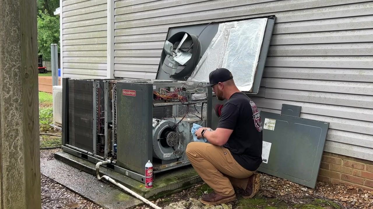 A technician uses a cloth to wipe down the blower motor, with a can of cleaner placed on the ground next to the unit.