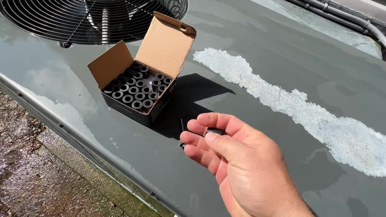 A hand holds a box of 1/4" Refrigerant Safety Locking Caps on top of the HVAC unit, with clear product labeling visible.
