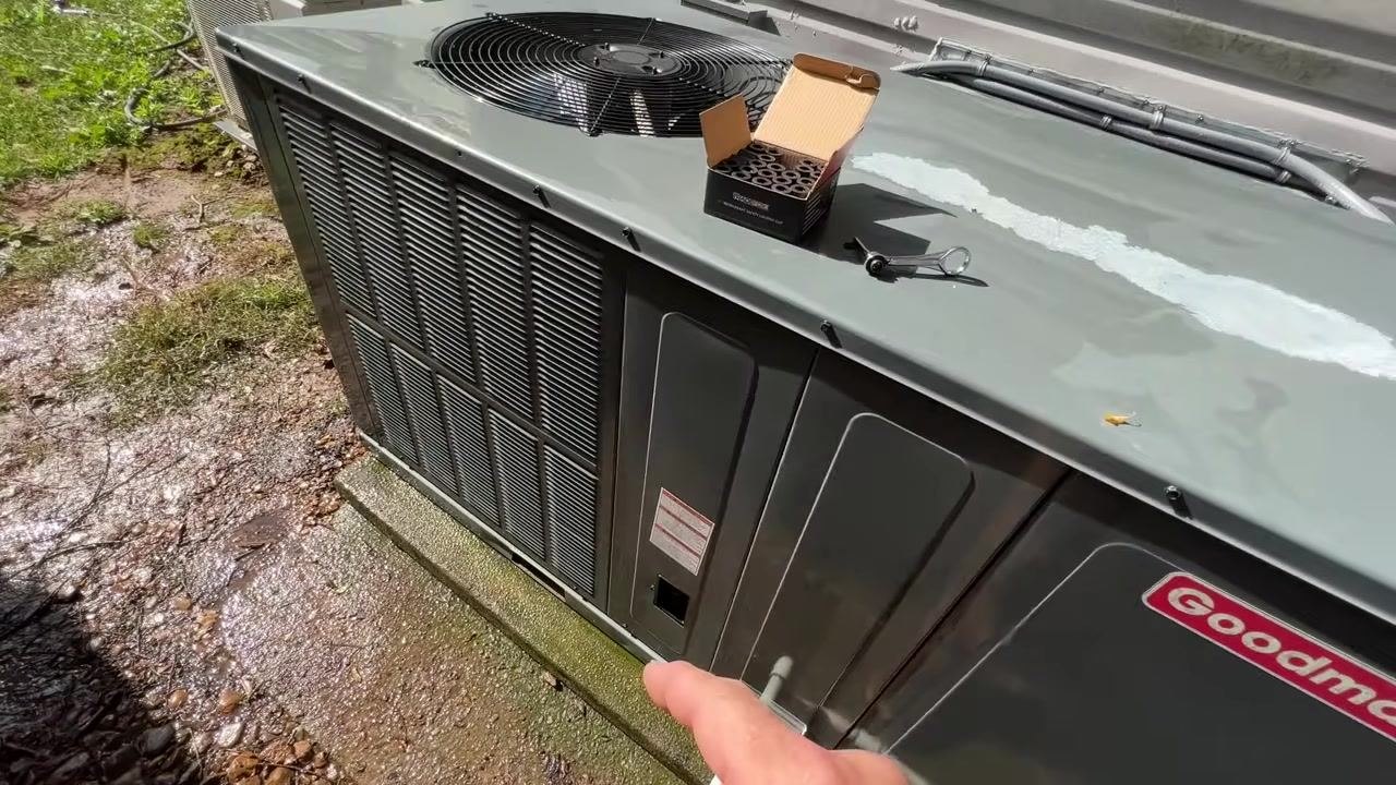 A hand holds a single black locking cap, with the open box of caps and a wrench on the HVAC unit's top panel.