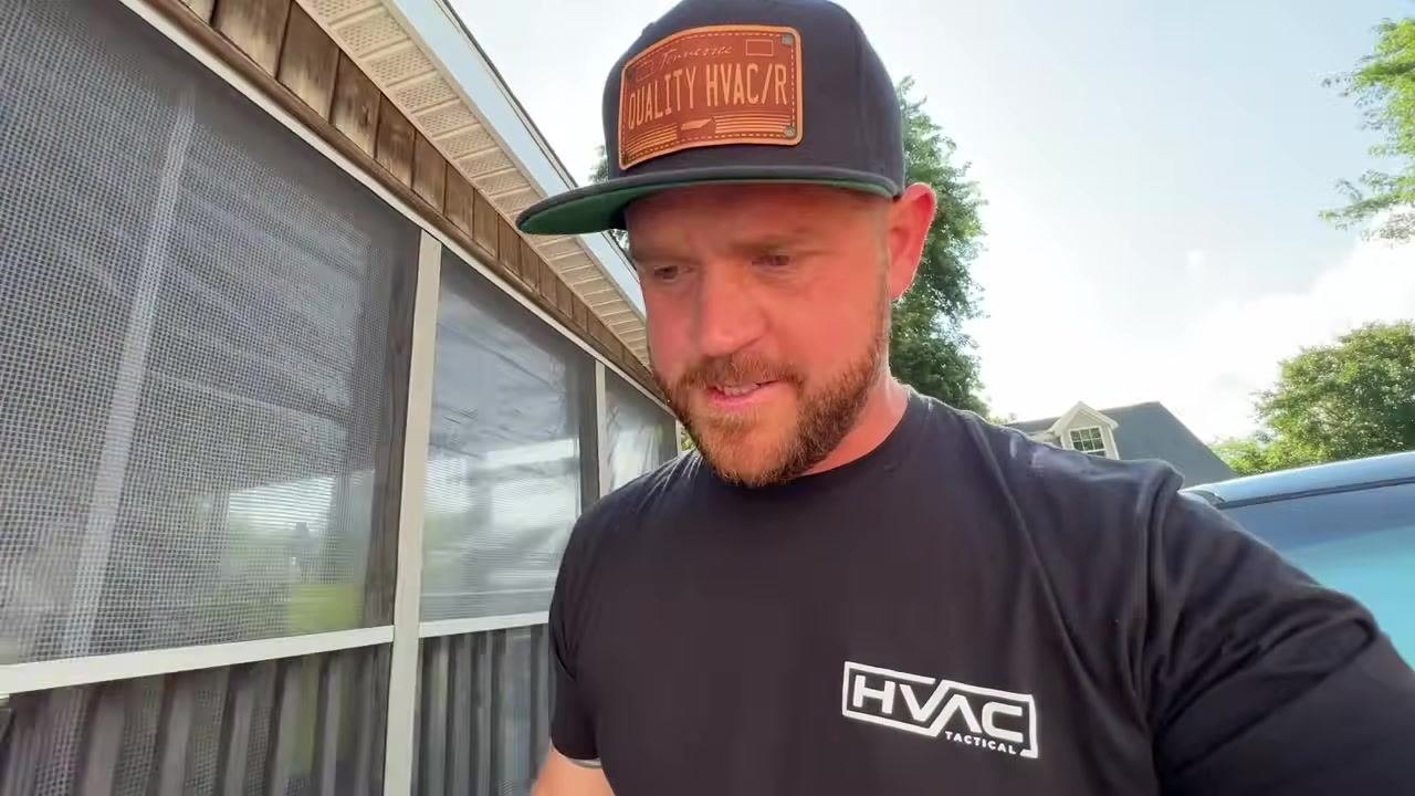 Technician smiling and gesturing, standing in a driveway with a house, vehicles, and trees in the background, encouraging feedback and subscriptions.