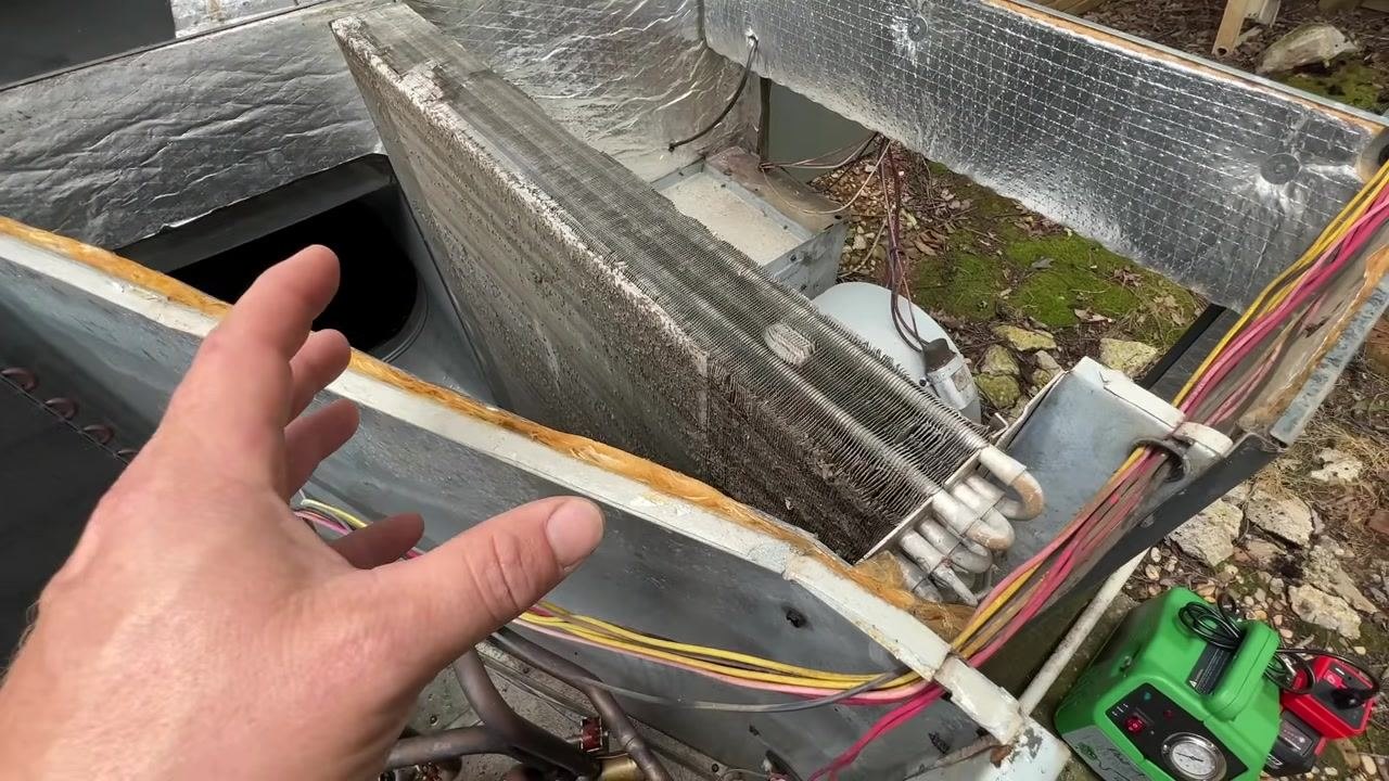 The open HVAC unit shows an exposed coil, with the green cleaning device and inverter ready for use nearby. Wires and insulation are visible.