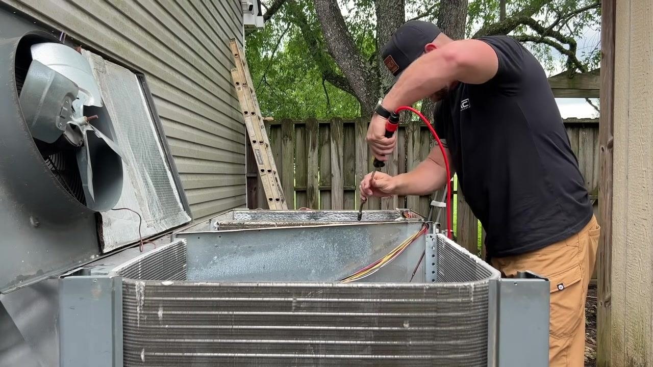 A technician continues spraying cleaner onto the coil, ensuring full coverage with foam.