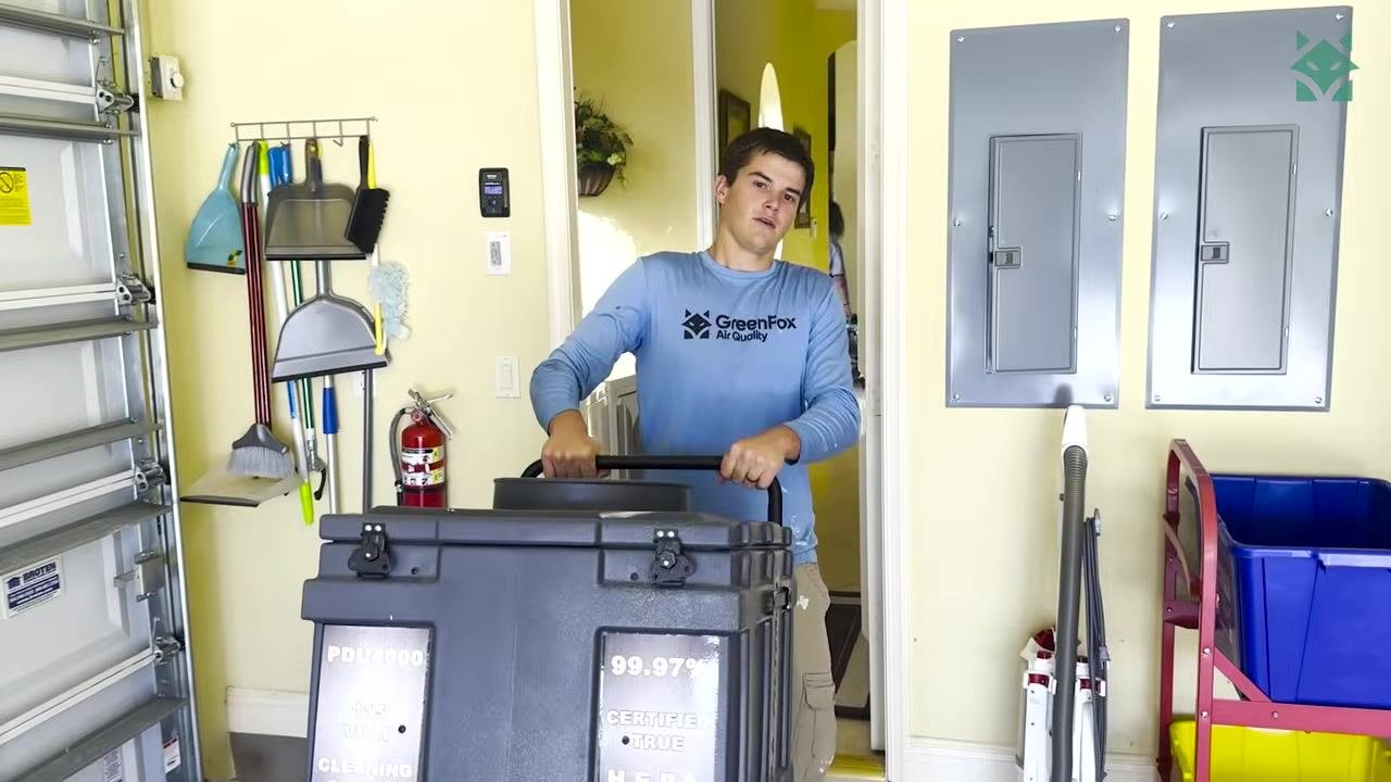 A technician inspects HVAC ductwork mounted near the ceiling in a utility room before cleaning begins.
