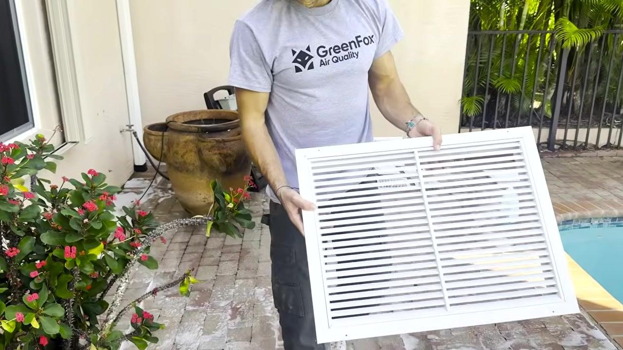 A technician holds up a freshly cleaned vent outdoors, ready for reinstallation.