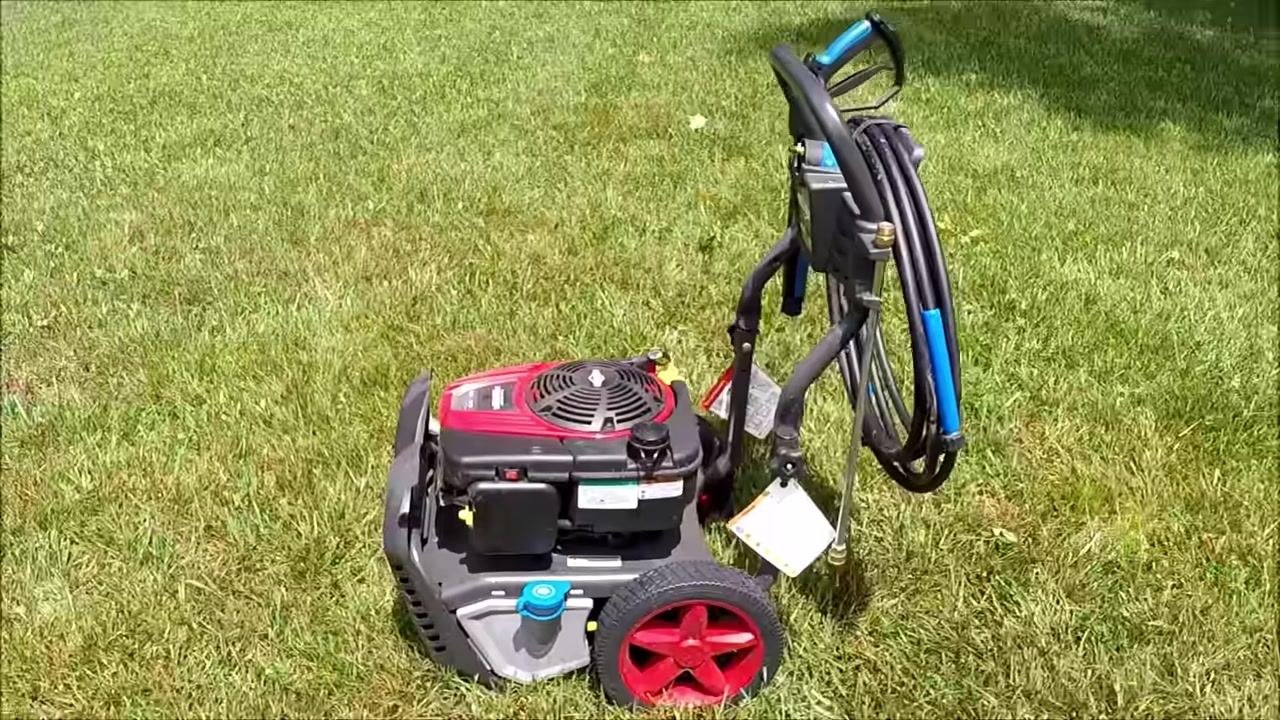Wide side view of the pressure washer, showing the full unit, hose, spray gun, and wheels on grass.